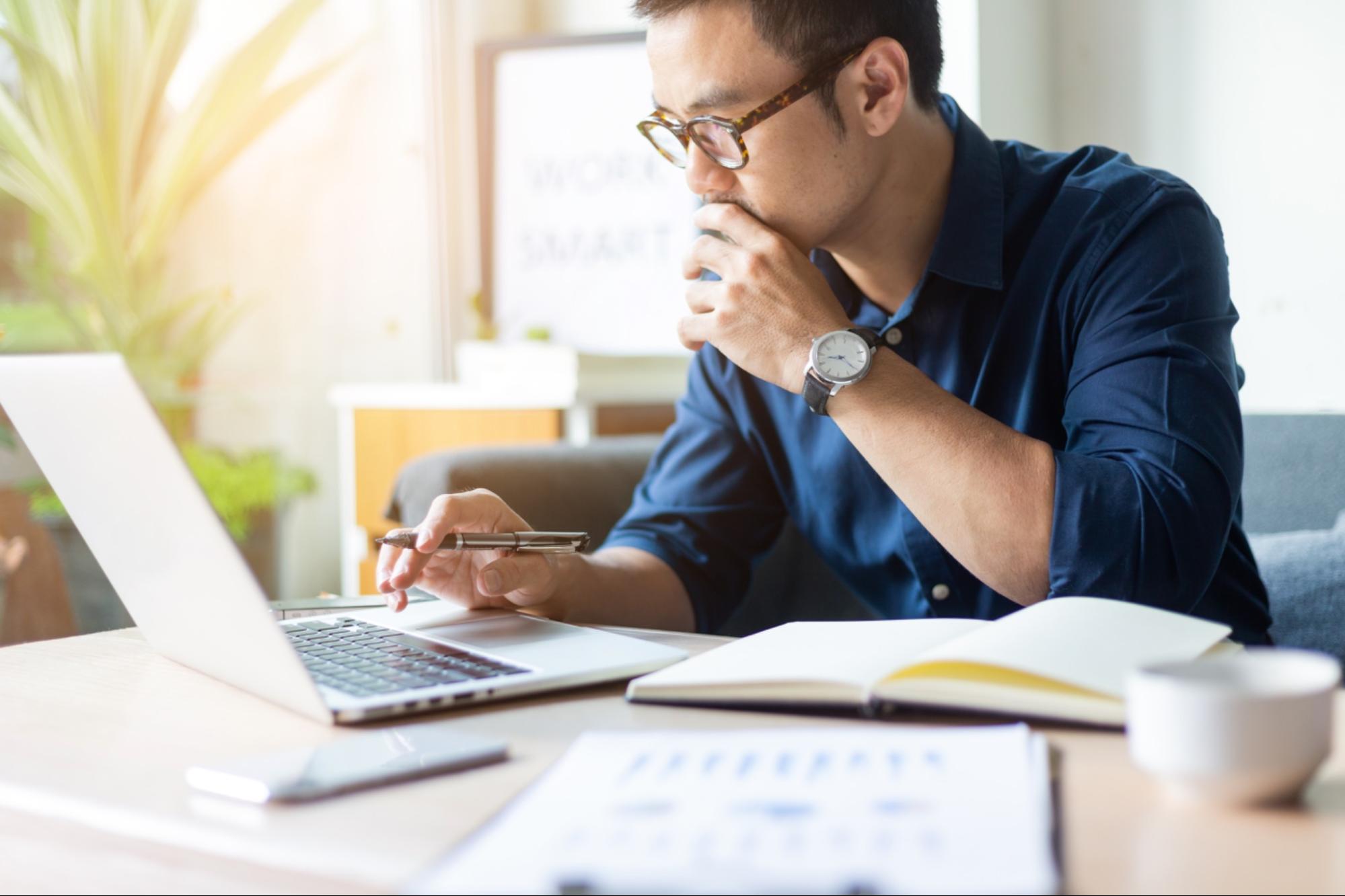 Person looking at laptop holding pen